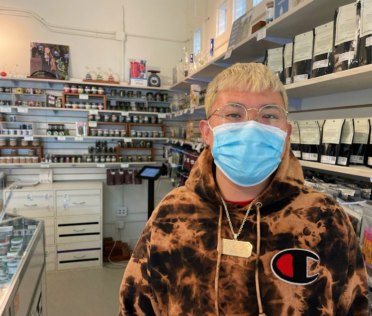 caption: Jeremy Mar works behind a glass counter lined with rows and rows of marijuana products at Hashtag Cannabis, a recreational retail shop near the Fremont bridge in Seattle. 