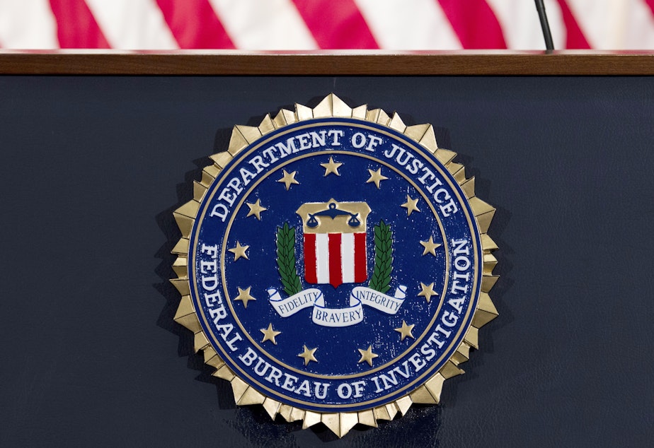 caption: The FBI seal is displayed on a podium. A former FBI agent is facing several charges tied to his work with a Russian oligarch.