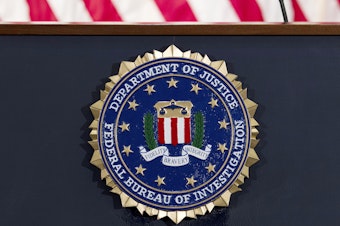 caption: The FBI seal is displayed on a podium. A former FBI agent is facing several charges tied to his work with a Russian oligarch.