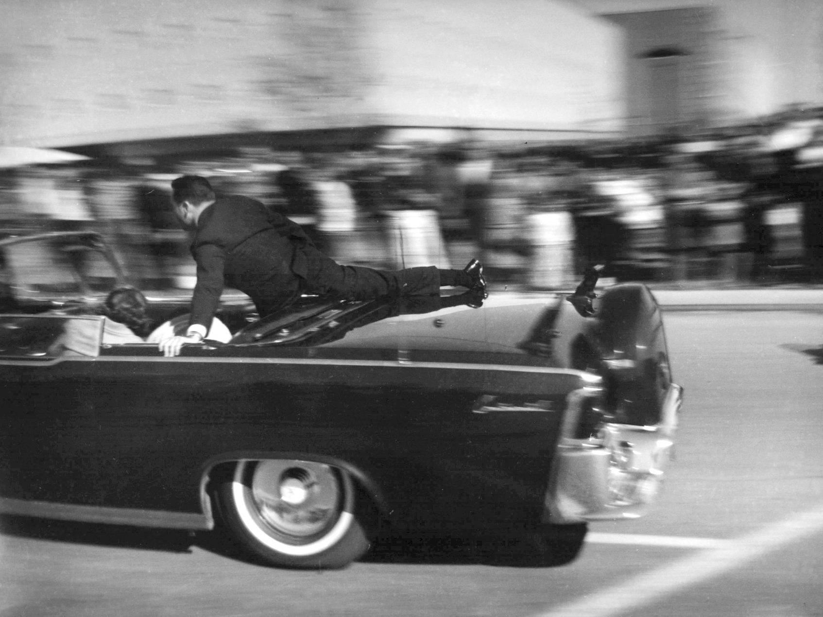 caption: Secret Service agent Clint Hill rides on the back of the presidential limousine moments after President John F. Kennedy was shot on Nov. 22, 1963.