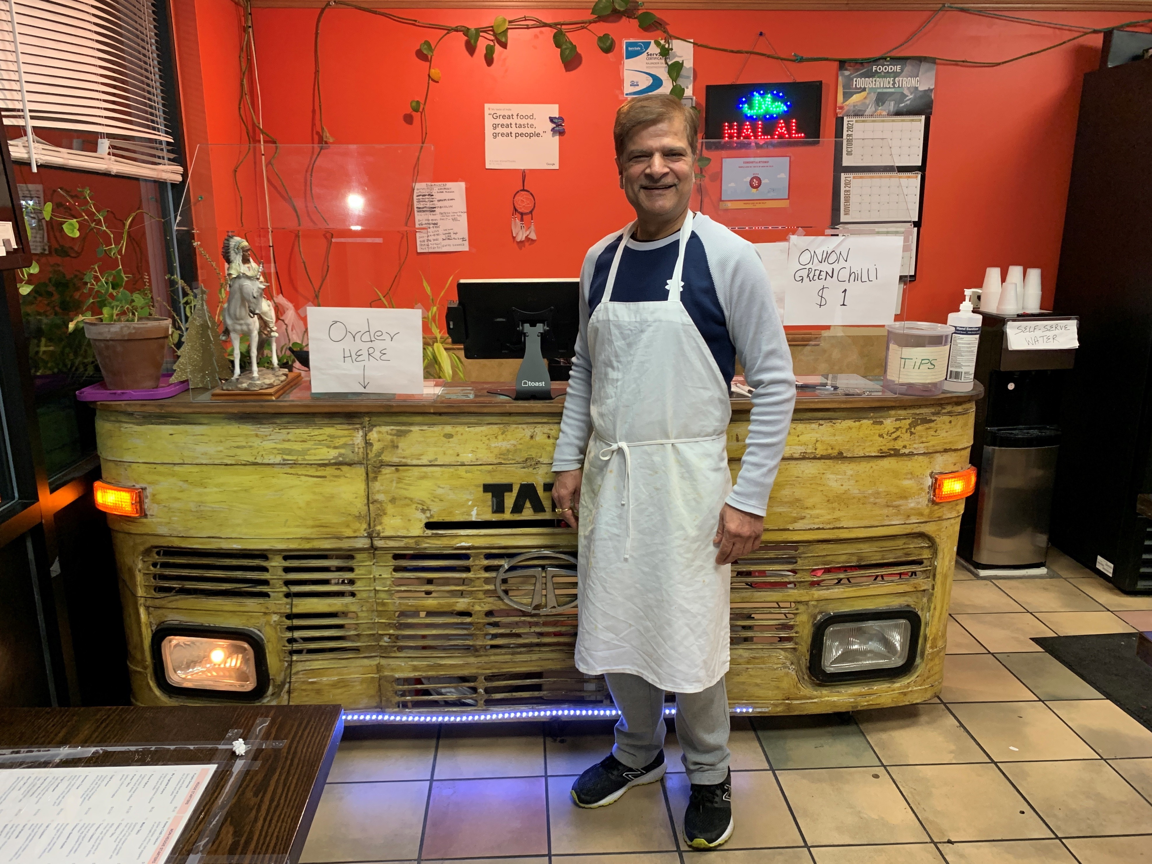 caption: Jagdeep Nayyar, owner and chef at My Taste of India, stands in front of the register stand that's made from the front panel of a real Tata truck — the best-selling brand in India.