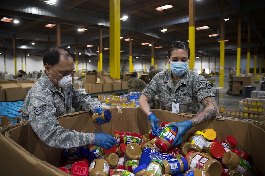 caption: Washington National Guard Airmen grab jars of peanut butter to add them to boxes along the assembly line at the Food Lifeline Covid Response Center on Tuesday, April 21, 2020,  along East Marginal Way South in Seattle.  