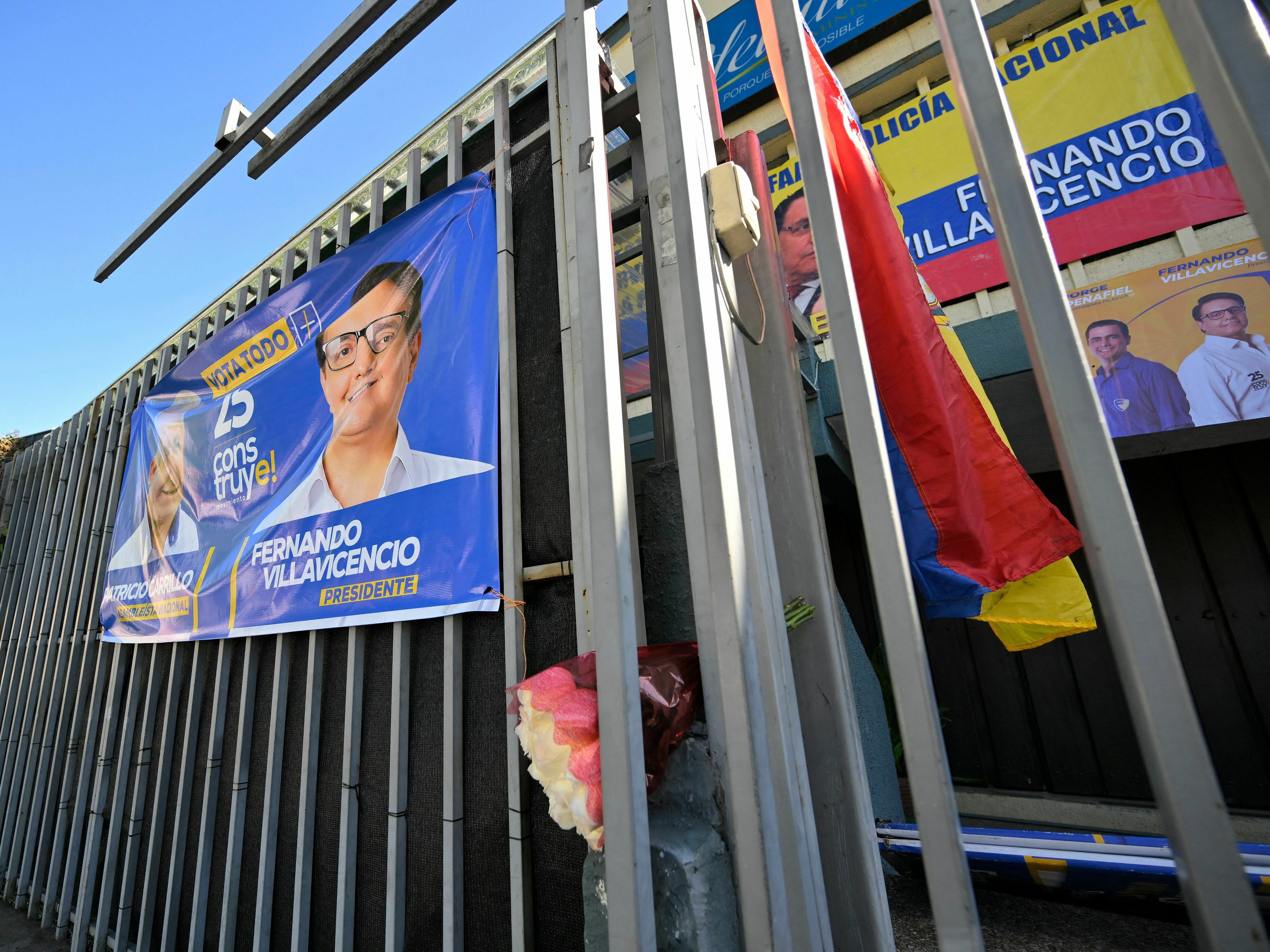 caption: An Ecuadorean flag and a bouquet of flowers are seen on the railings of the sports complex where Ecuadorean presidential candidate Fernando Villavicencio was assassinated on the eve, in Quito on August 10, 2023.