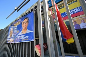 caption: An Ecuadorean flag and a bouquet of flowers are seen on the railings of the sports complex where Ecuadorean presidential candidate Fernando Villavicencio was assassinated on the eve, in Quito on August 10, 2023.