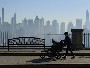 caption: Amazon and Target are among the latest big retailers to stop selling weighted infant sleepwear due to concerns about safety. Here, a woman pushes a stroller as the New York skyline is seen from Weehawken, New Jersey.