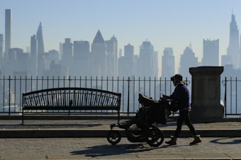 caption: Amazon and Target are among the latest big retailers to stop selling weighted infant sleepwear due to concerns about safety. Here, a woman pushes a stroller as the New York skyline is seen from Weehawken, New Jersey.