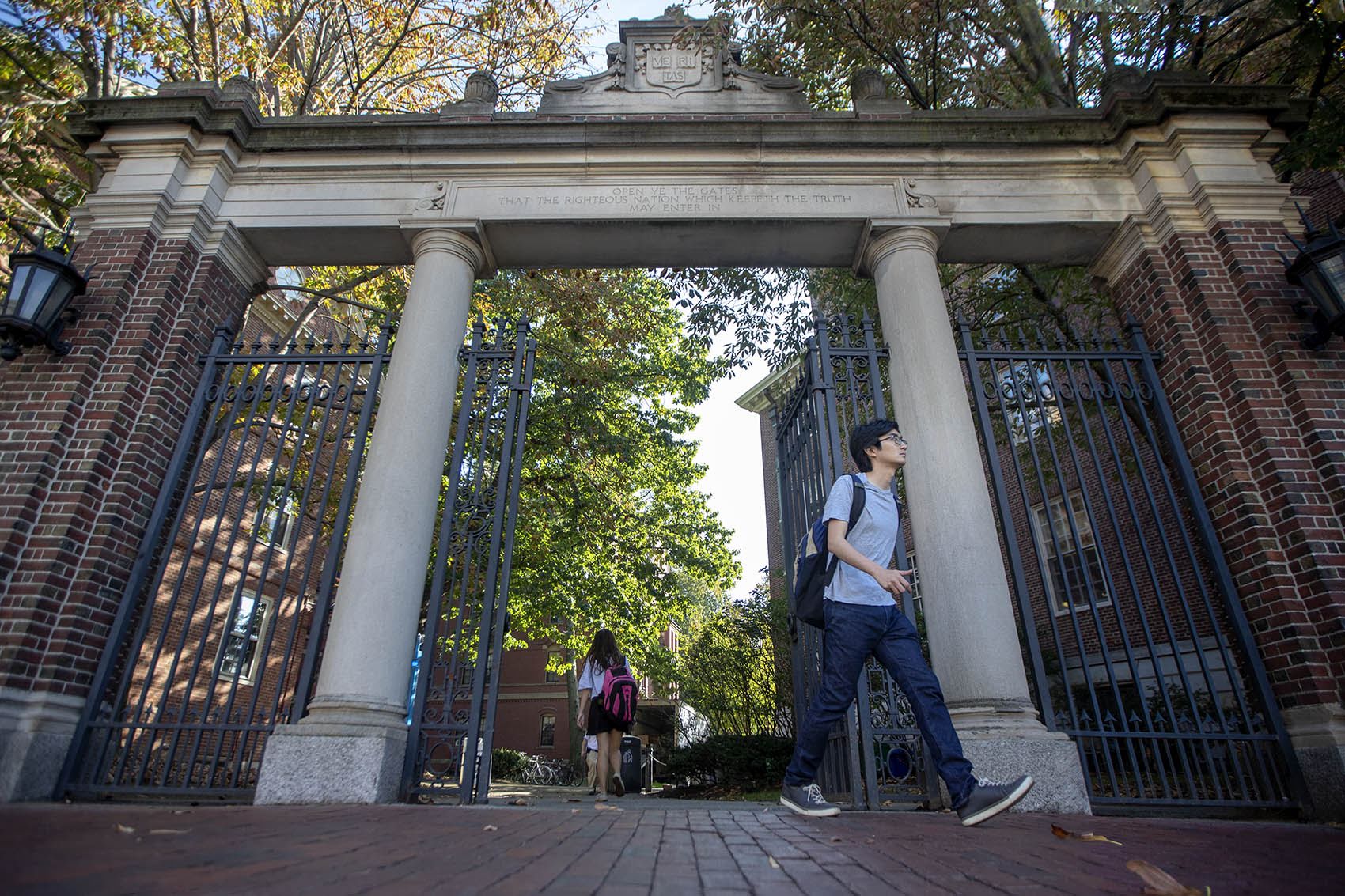 caption: Harvard students walk through the Class of 1875 Gate in Harvard Yard. (Jesse Costa/WBUR)