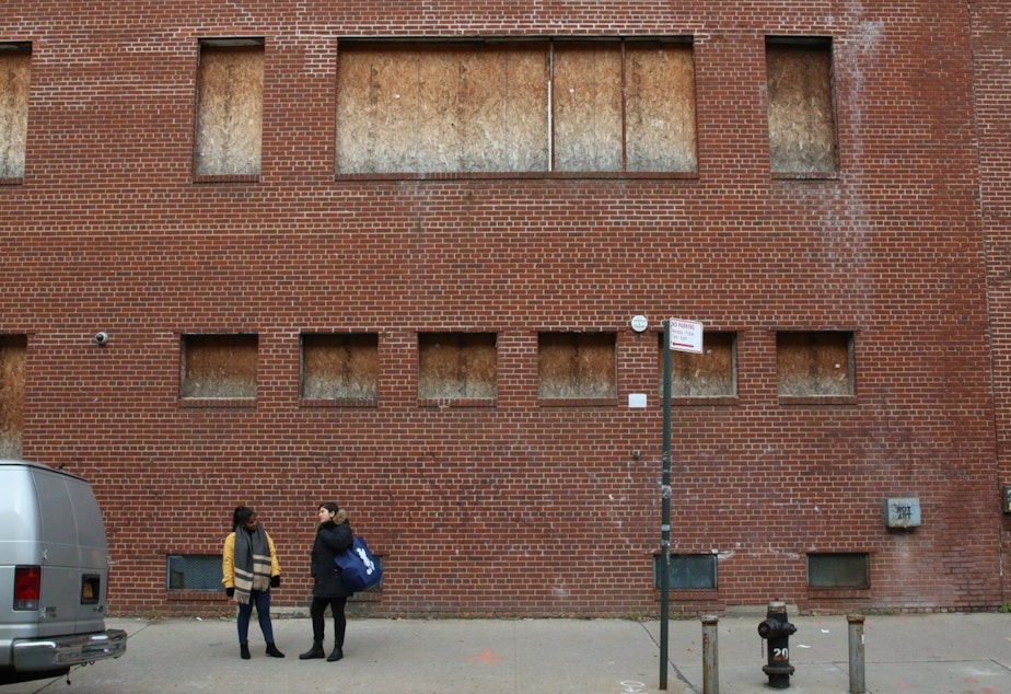 caption: Lena Afridi and Sabrina Jalal stand before a boarded up Queens building on property Amazon will occupy.