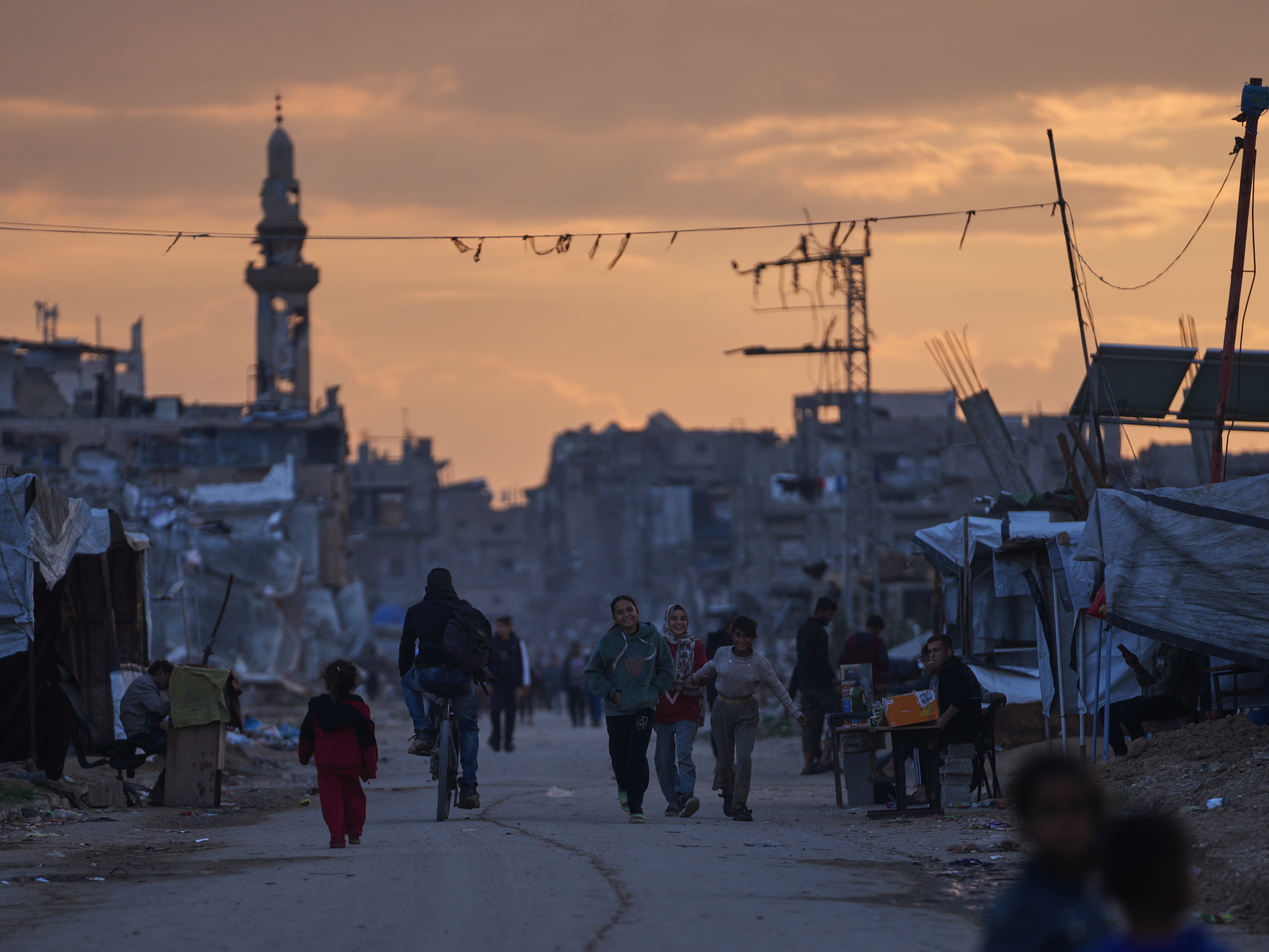 caption: Palestinian youth walk along a tent camp for displaced people as the sun sets in Nuseirat, central Gaza Strip, Friday, Dec. 26, 2025.