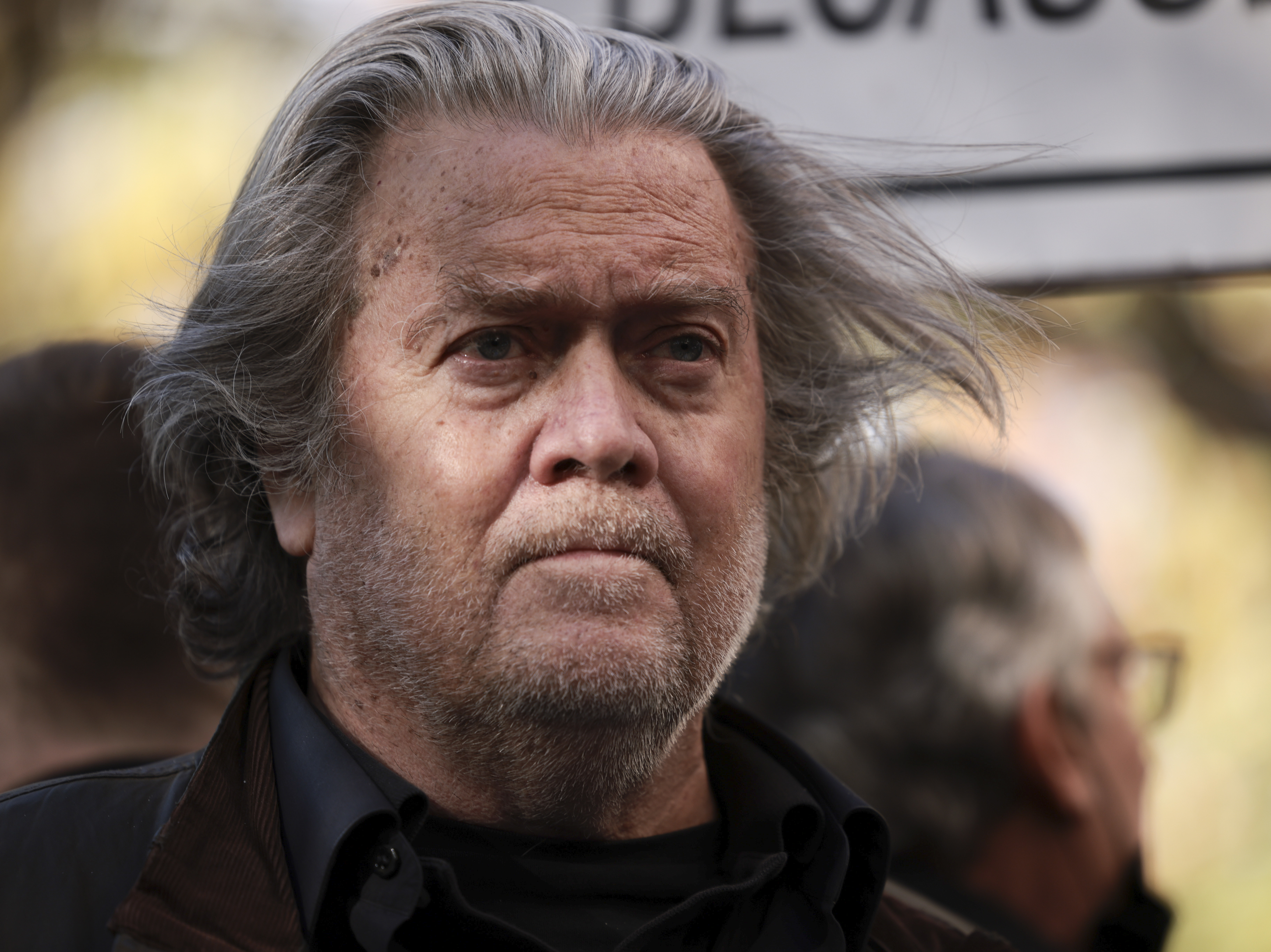 caption: Former Trump administration White House adviser Steve Bannon listens as attorney David Schoen speaks to reporters outside of the E. Barrett Prettyman Federal District Court House on Nov. 15, 2021.