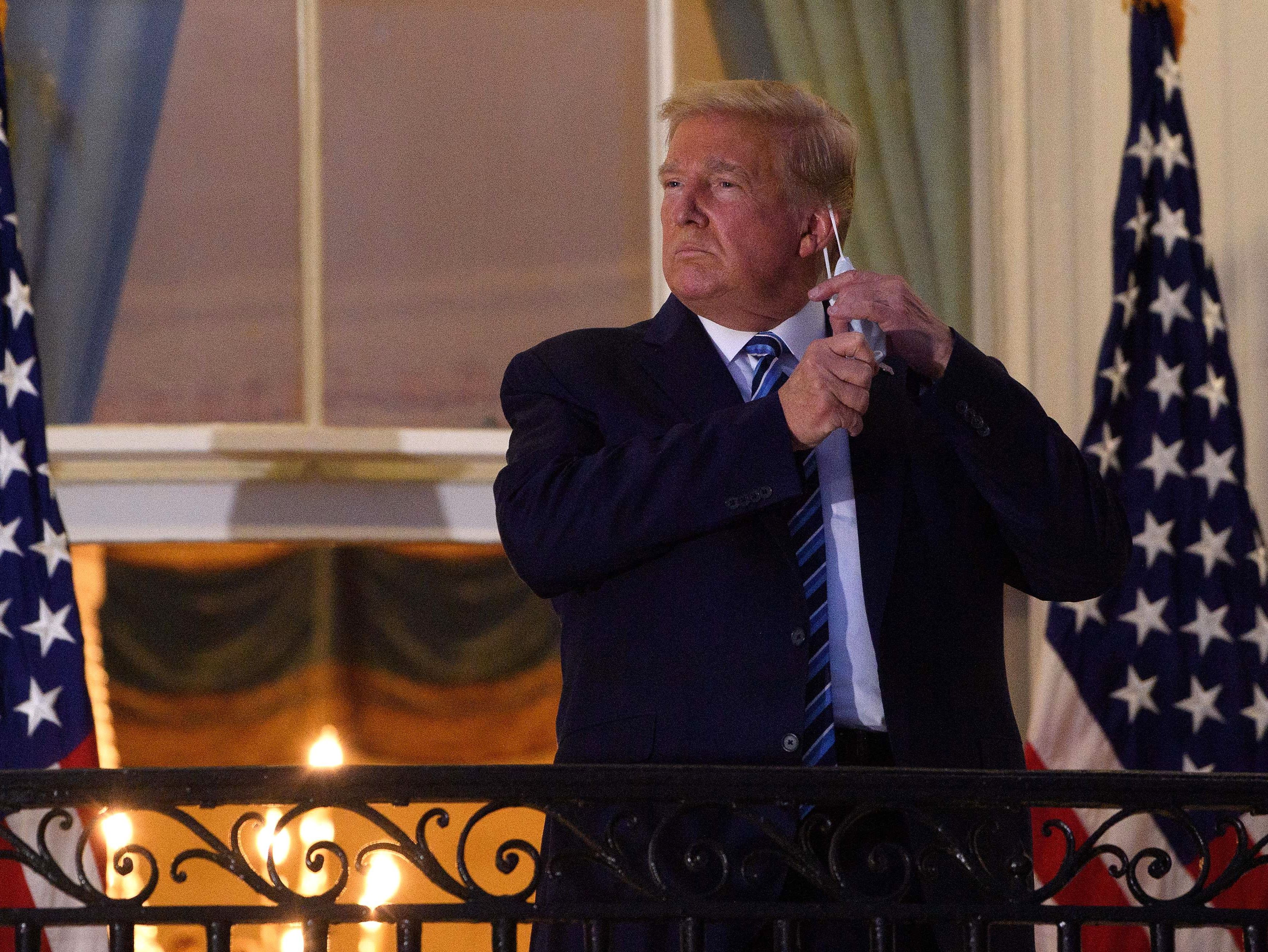 caption: President Trump takes off his face mask as he arrives at the White House upon his return from Walter Reed National Military Medical Center on Monday.