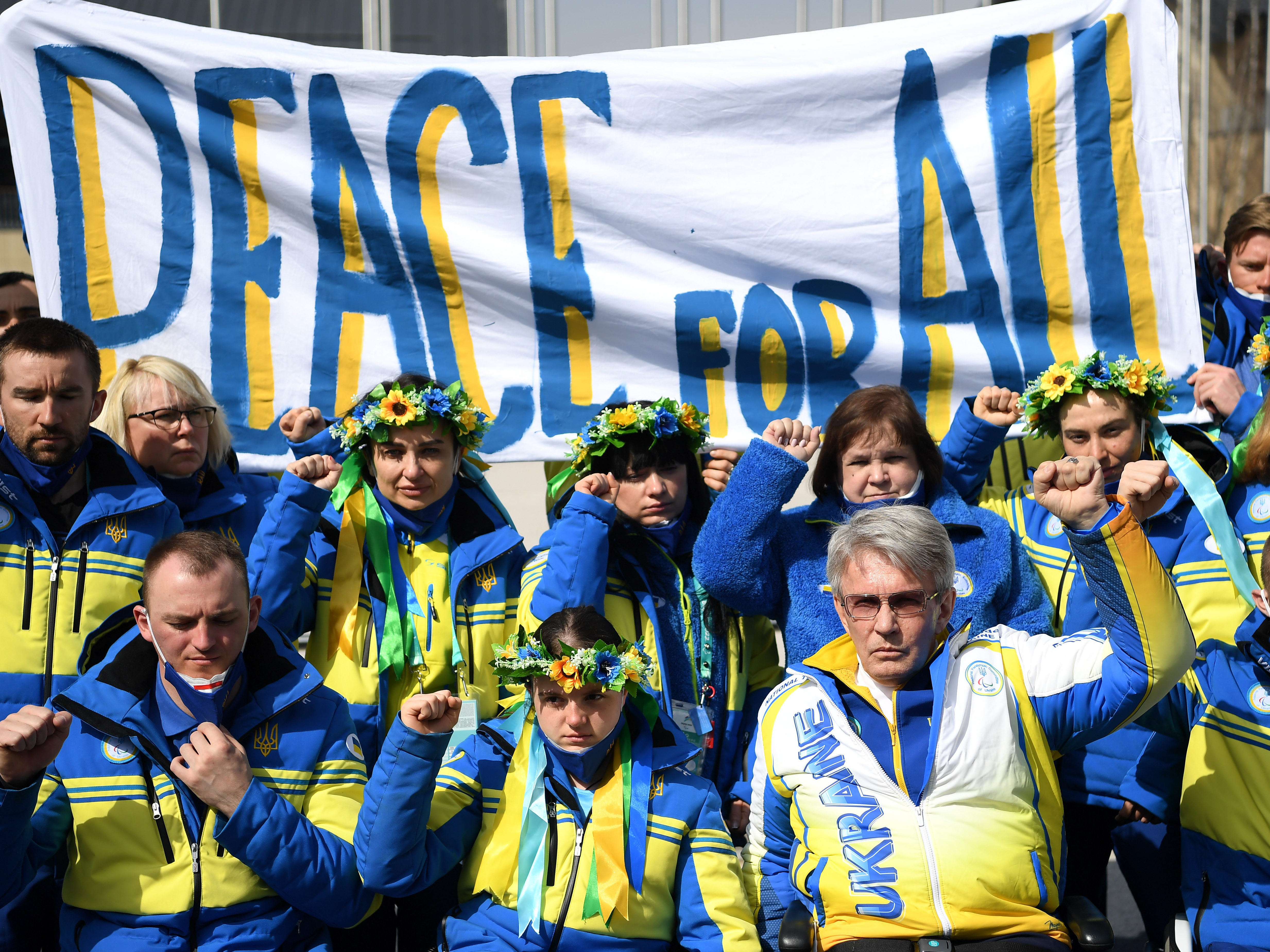 caption: President of Ukraine's Paralympic Committee Valerii Sushkevych and members of Team Ukraine hold a banner up reading "Peace for All" in the Athletes Village during day six of the Beijing 2022 Winter Paralympics.