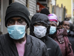 caption: People wait for a distribution of masks and food from the Rev. Al Sharpton in Harlem on Saturday after a new state mandate was issued requiring residents to wear face coverings in public due to COVID-19.