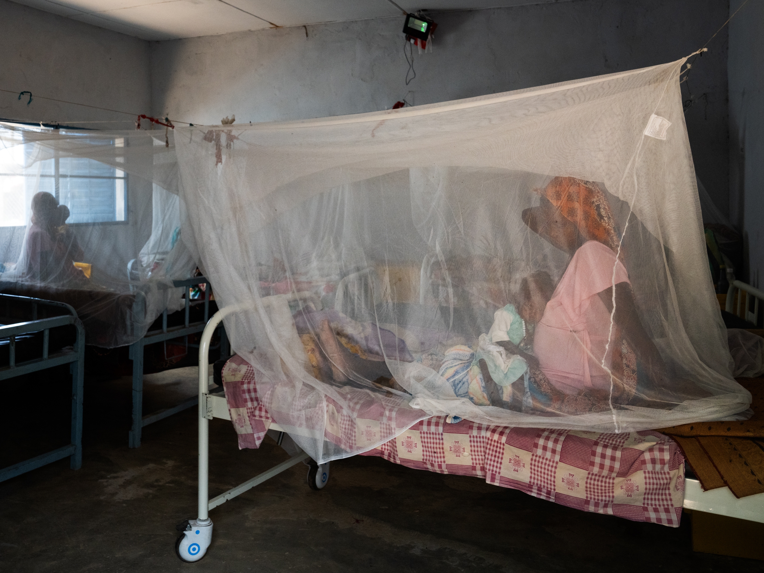 caption: A pregnant woman brought her child to a health clinic in Farchana, Chad. They are sitting under a mosquito net. MIdwives play a critical role in addressing the country's high rate of maternal mortality.