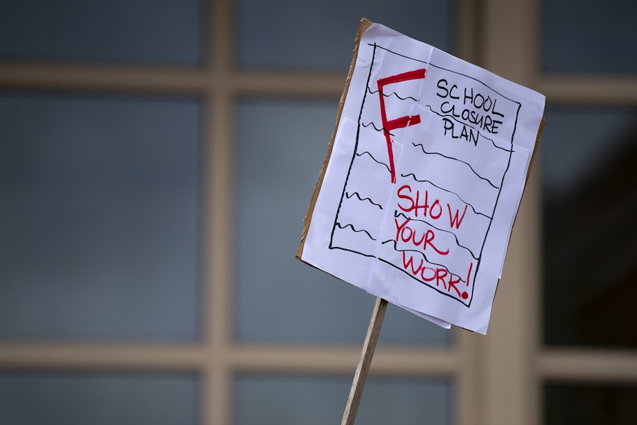caption: Erin MacDougall holds a sign while attending an ‘All Together for Seattle Schools’ rally ahead of a Seattle Public Schools school closures meeting on Tuesday, May 28, 2024, at Roosevelt high school in Seattle. 