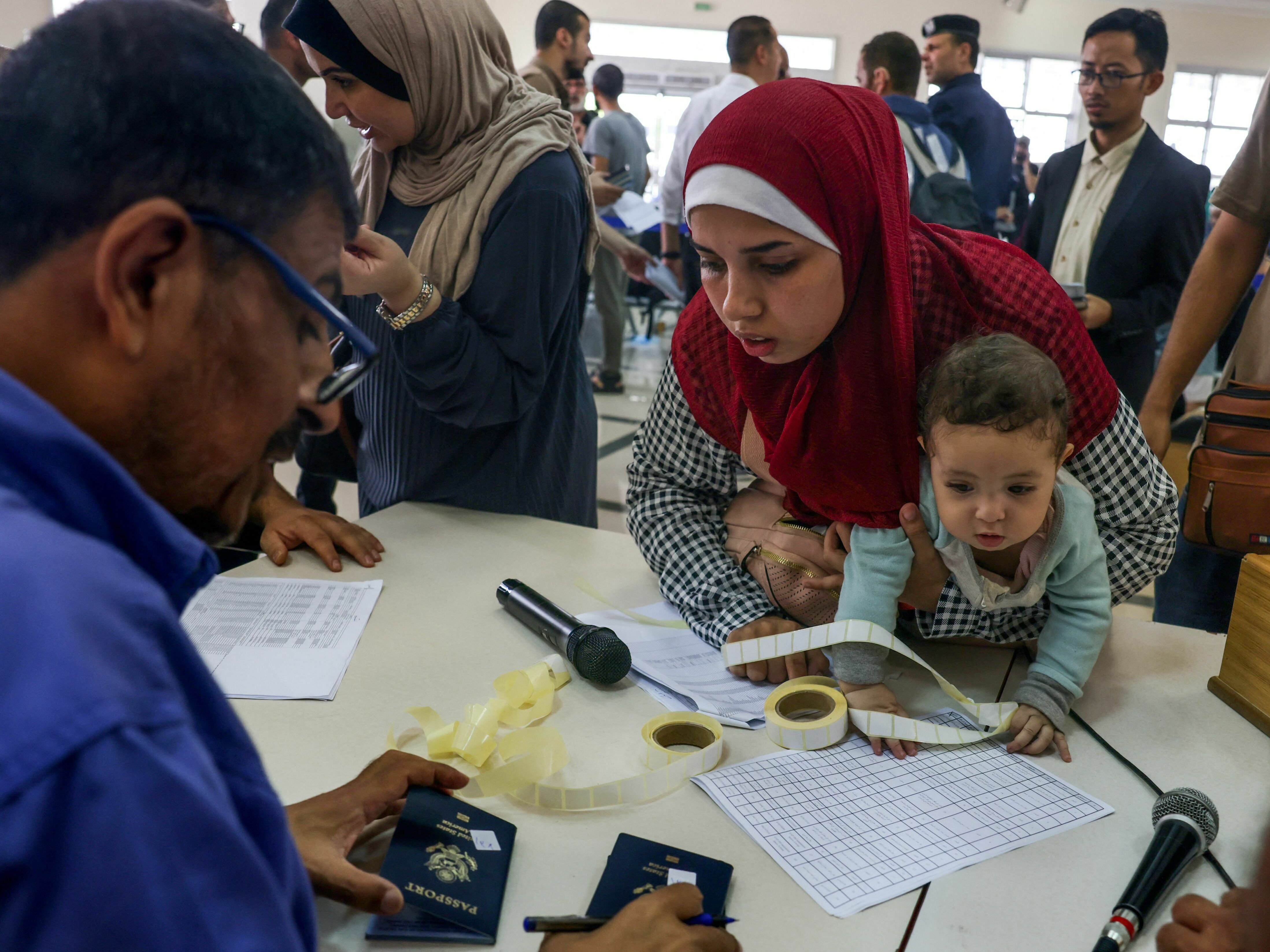 caption: Civilians leaving Gaza display their documents as dual national Palestinians and foreigners prepare to cross the Rafah border point with Egypt, in the southern Gaza Strip, on  Thursday.