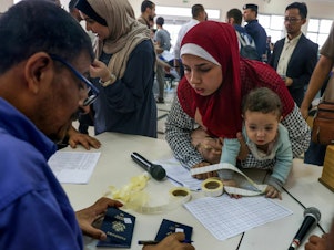 caption: Civilians leaving Gaza display their documents as dual national Palestinians and foreigners prepare to cross the Rafah border point with Egypt, in the southern Gaza Strip, on  Thursday.