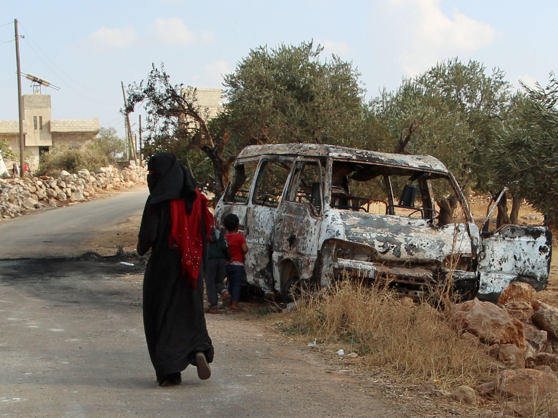 caption: A woman walks past a wrecked van near the northwestern Syrian village of Barisha. Local residents and medical staff tell NPR that noncombatant civilians were killed and injured in the van the night of the U.S. raid on the compound of ISIS leader Abu Bakr al-Baghdadi.