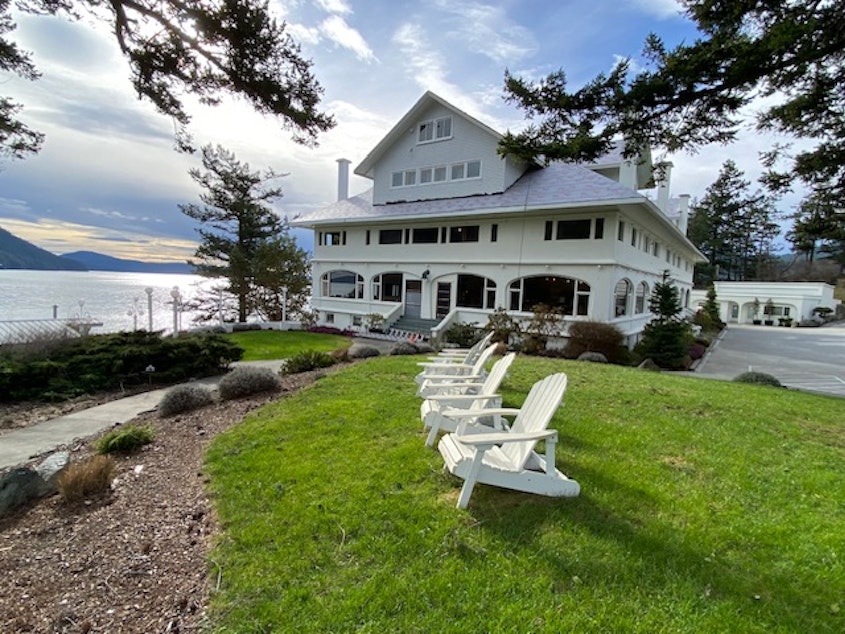 caption: A row of Adirondack chairs overlook Cascade Bay with Moran Mansion in the background on Orcas Island, Washington.