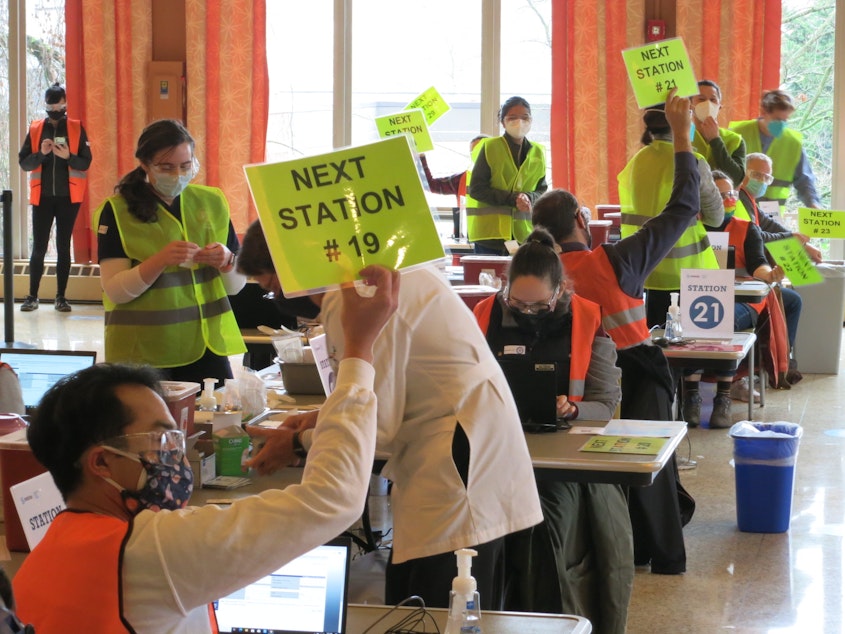 caption: Workers hold up signs indicating they're ready to vaccinate another patient at a mass vaccination site run by Swedish at Seattle University, Saturday, January 16, 2021. 