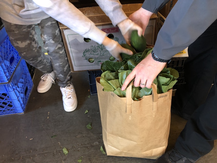 caption: A volunteer at Rainier Valley Food Bank fills a bag with produce. Local food banks are seeing a jump in demand as people struggle to make ends meet. 