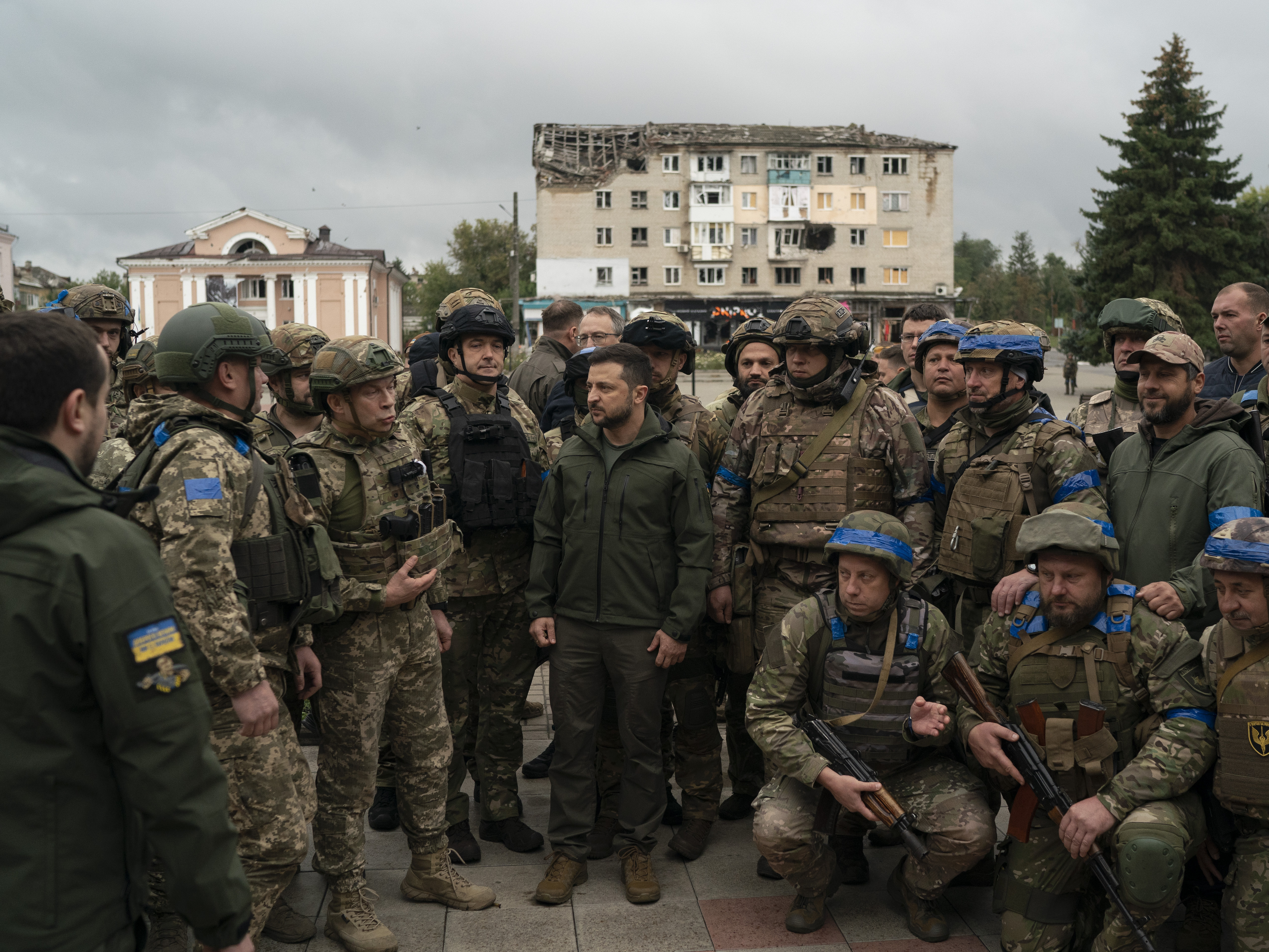 caption: Ukrainian President Volodymyr Zelenskyy stands with soldiers after attending a national flag-raising ceremony in Izium, Ukraine, on Wednesday. Zelenskyy thanked soldiers for their efforts in retaking the area, as the Ukrainian flag was raised in front of the burned-out city hall building.