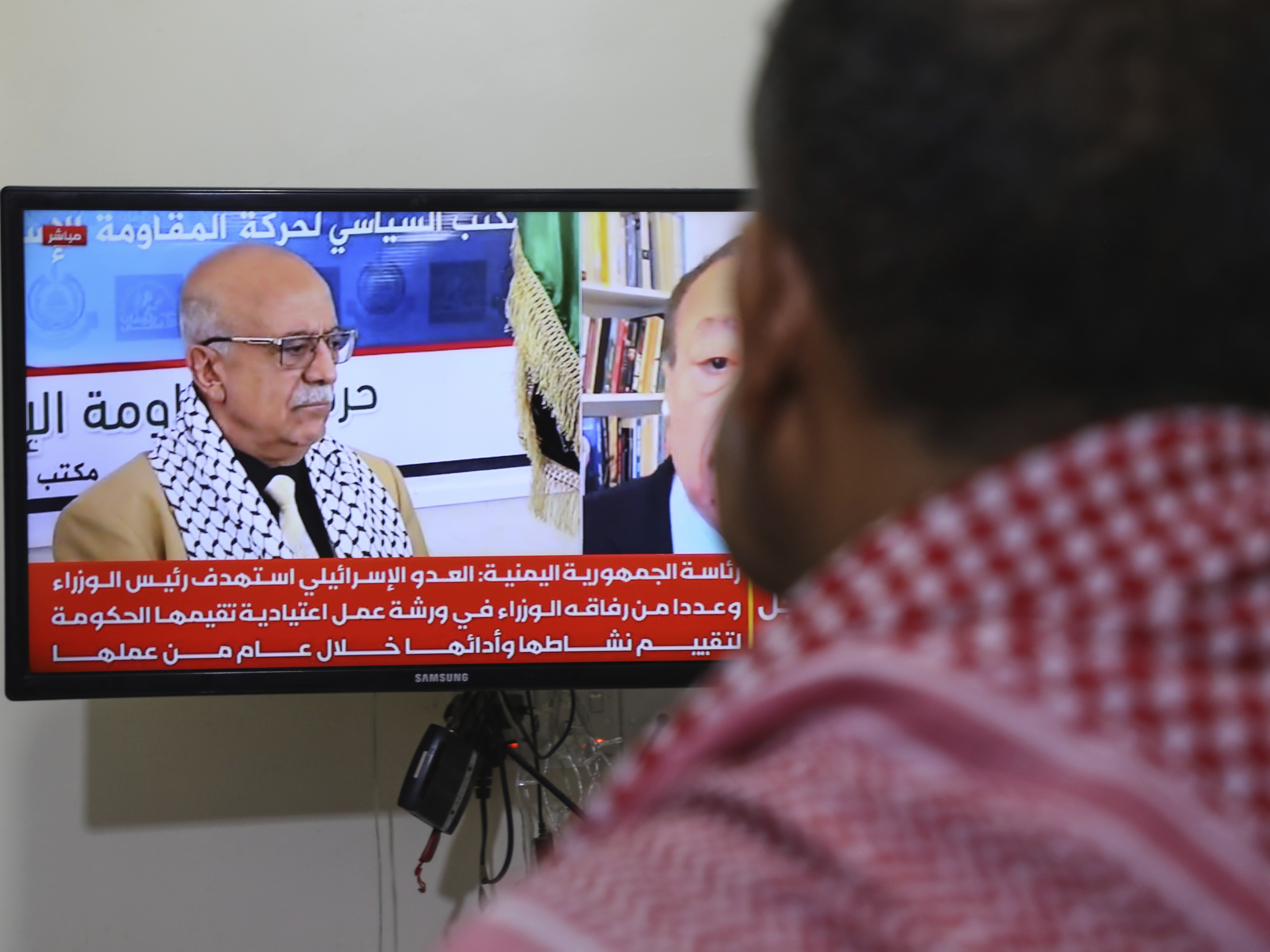 caption: A man watches the news on TV, displaying footage of Ahmed al-Rahawi, the prime minister of the Houthi-controlled government, who was killed, along with others, in Thursday's Israeli strikes on the capital, in Sanaa, Yemen, Saturday, Aug. 30, 2025.