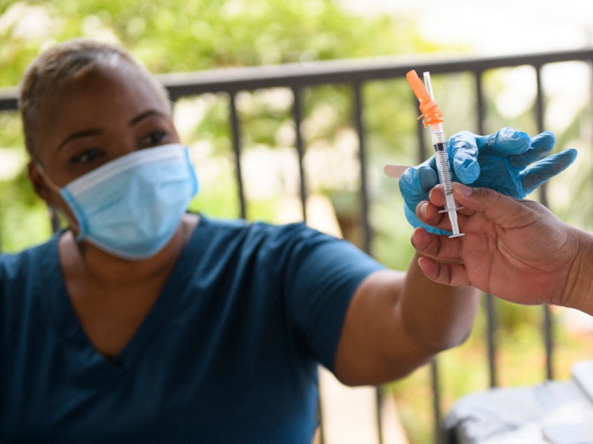 caption: A nurse is handed a dose of the Pfizer Covid-19 vaccine before administering it to a college student during a mobile vaccination clinic at the California State University, Long Beach, on Aug. 11.