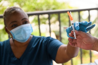 caption: A nurse is handed a dose of the Pfizer Covid-19 vaccine before administering it to a college student during a mobile vaccination clinic at the California State University, Long Beach, on Aug. 11.