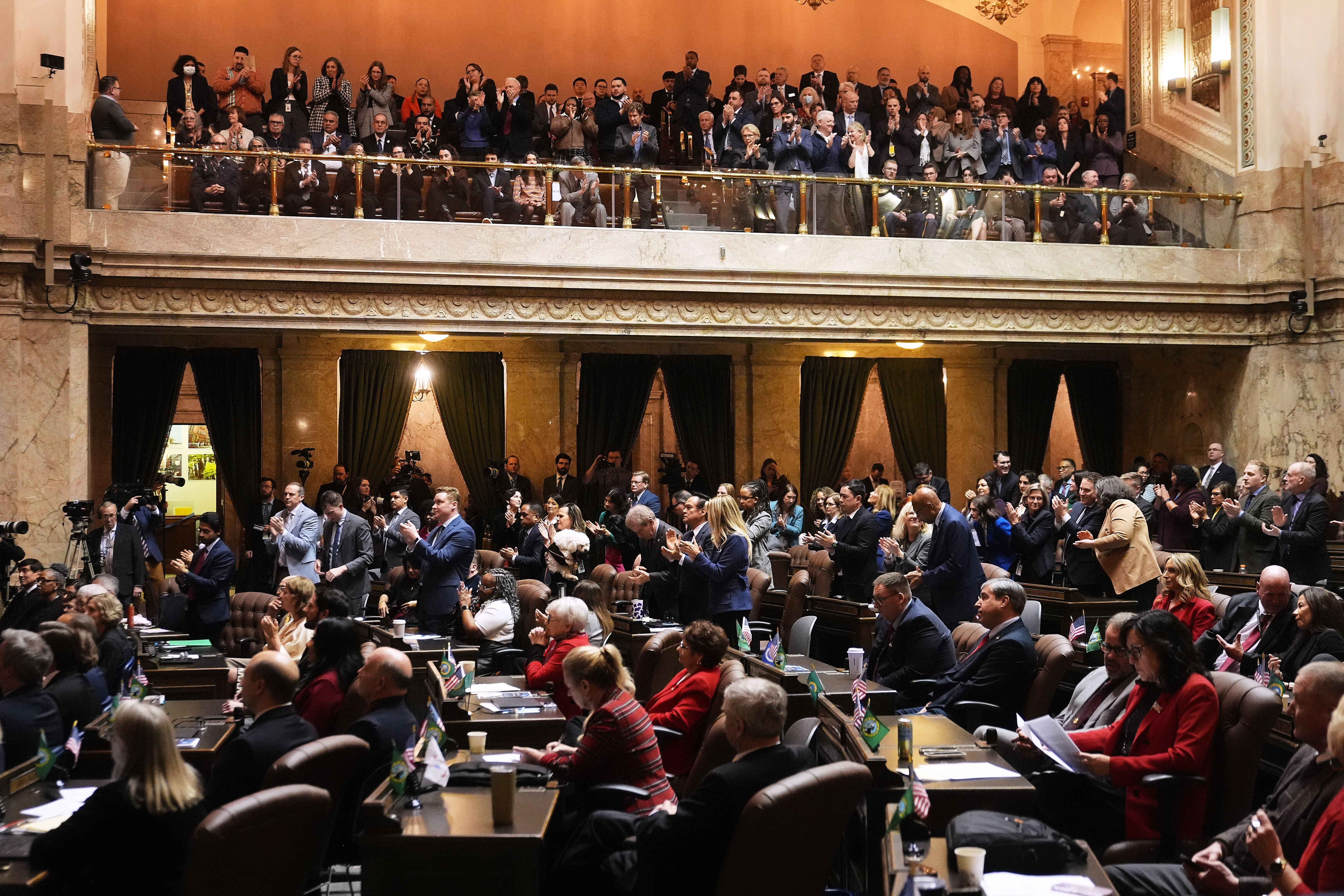 caption: Democrats and visitors in the gallery stand to clap as Republicans stay seated while Washington Gov. Bob Ferguson delivers his State of the State address during a joint legislative session at the Washington State Capitol, Tuesday, Jan. 13, 2026, in Olympia, Wash.