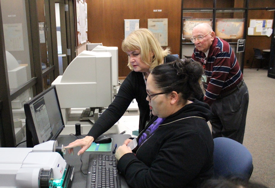 caption: Chelsea Craig, seated, looks through microfilm in the public research room of the National Archives in Seattle. A member of the Tulalip Tribes, Craig is searching for documents about the tribe's history. She is assisted by volunteers Janice Hemingway and Dick Hall.