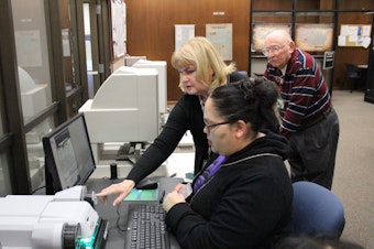 caption: Chelsea Craig, seated, looks through microfilm in the public research room of the National Archives in Seattle. A member of the Tulalip Tribes, Craig is searching for documents about the tribe's history. She is  assisted by volunteers Janice Hemingway and Dick Hall.