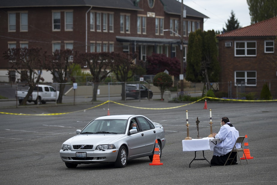 caption: Soledad Colmenares speaks with Father Jose Alvarez during walk and drive through confessions on Friday, April 24, 2020, in the parking lot at Holy Family Roman Catholic Church in White Center. 