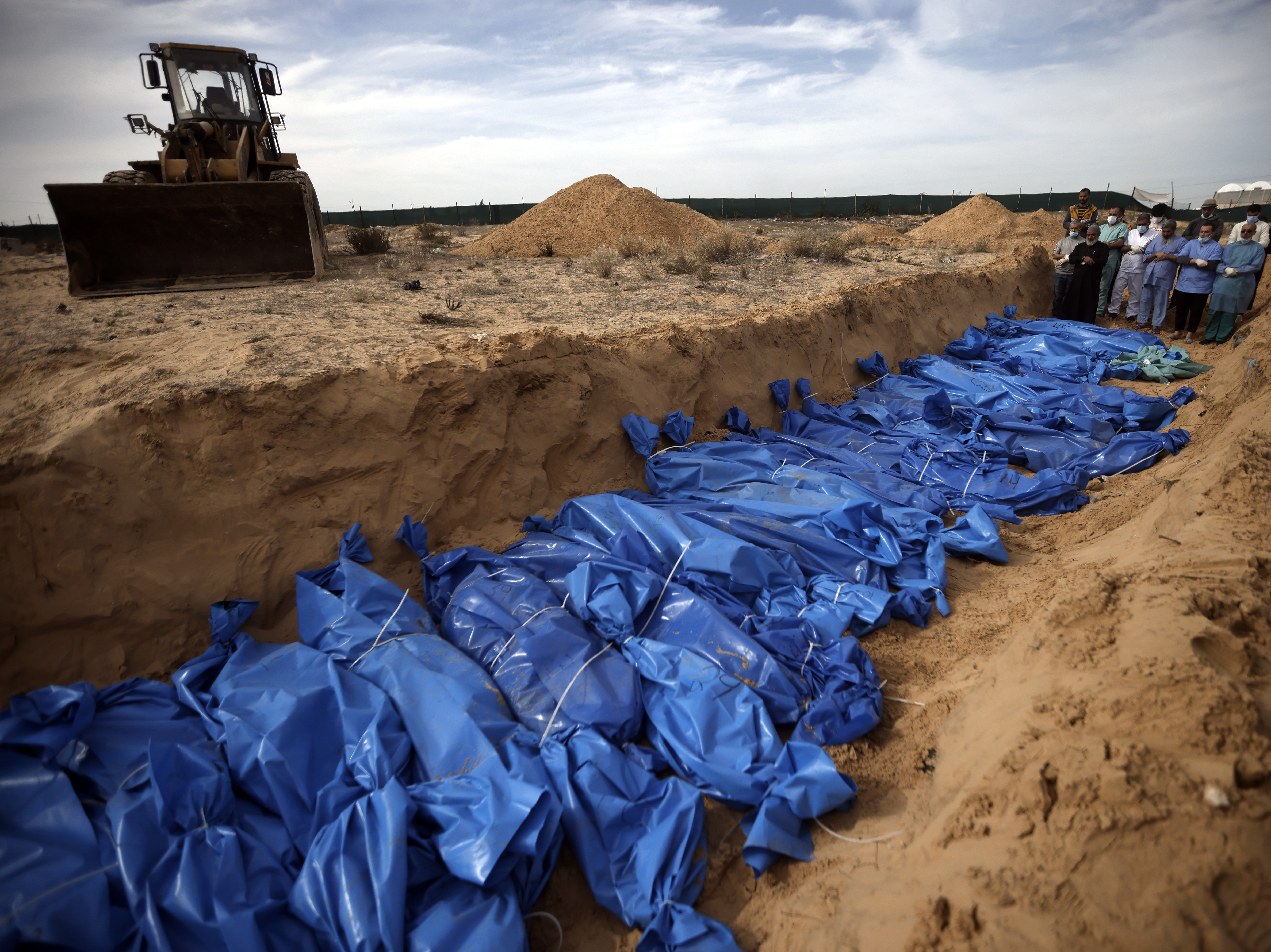 caption: Palestinians pray over bodies of people killed in an Israeli bombardment, brought from the Shifa hospital, before burying them in a mass grave in the town of Khan Younis, southern Gaza Strip, Nov. 22.