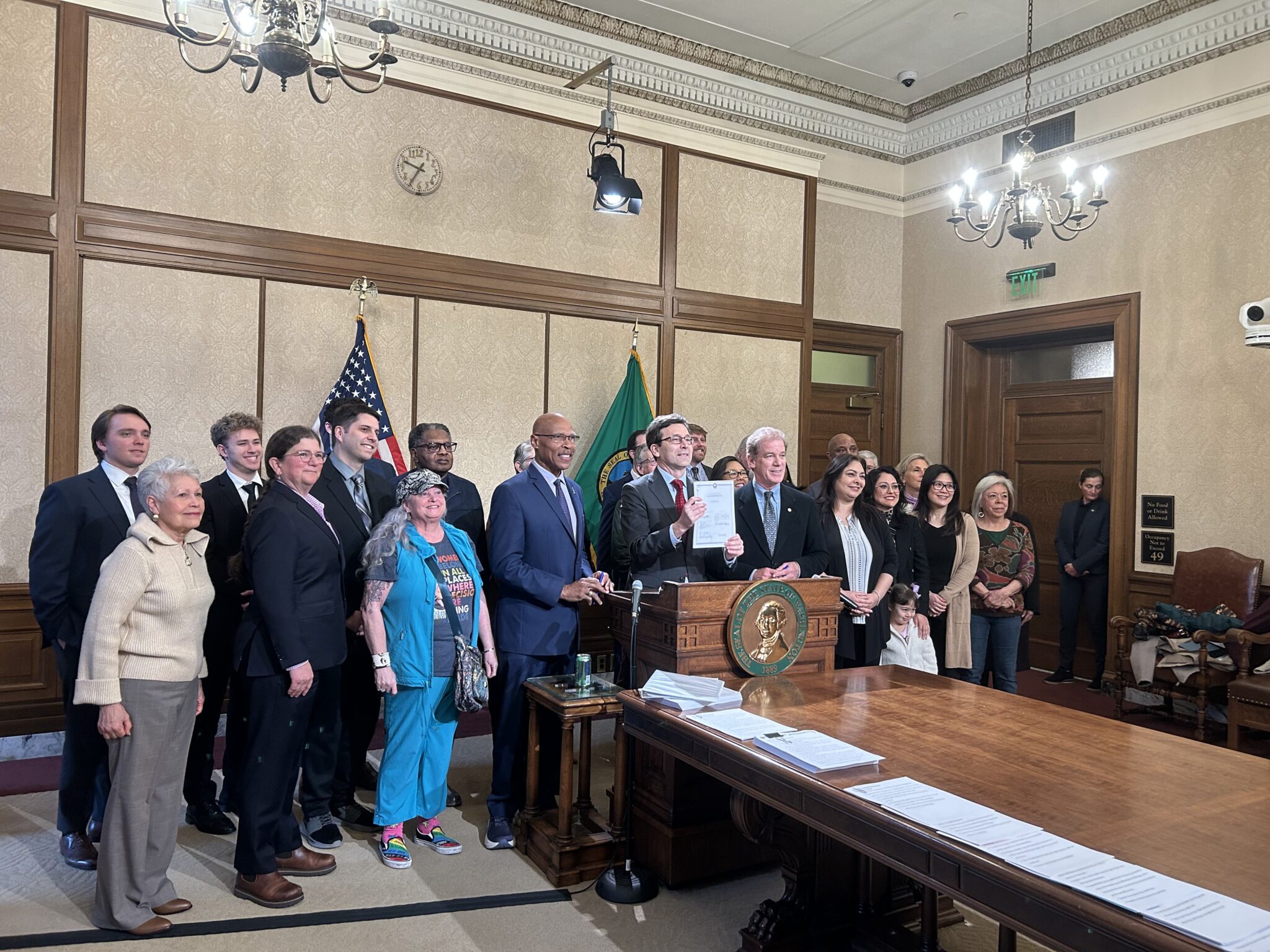 caption: Gov. Bob Ferguson holds up Senate Bill 5974, which sets heightened standards for sheriffs, alongside lawmakers and advocates after signing it on Wednesday, April 1, 2026, in Olympia, Washington. 