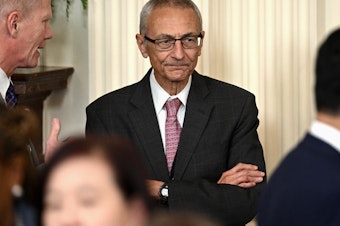 caption: John Podesta looks on during a meeting between President Biden and mayors at the White House on Jan. 19, 2024.