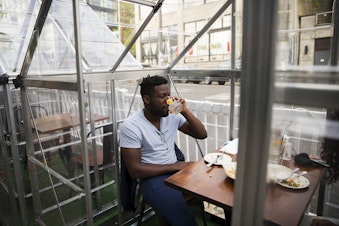 caption: Plum Bistro diner Anta, left, takes a sip of his drink while dining inside of a clear structure on Wednesday, May 5, 2021, at the restaurant in Seattle's Capitol Hill neighborhood.