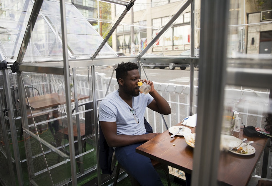 caption: Plum Bistro diner Anta, left, takes a sip of his drink while dining inside of a clear structure on Wednesday, May 5, 2021, at the restaurant in Seattle's Capitol Hill neighborhood.