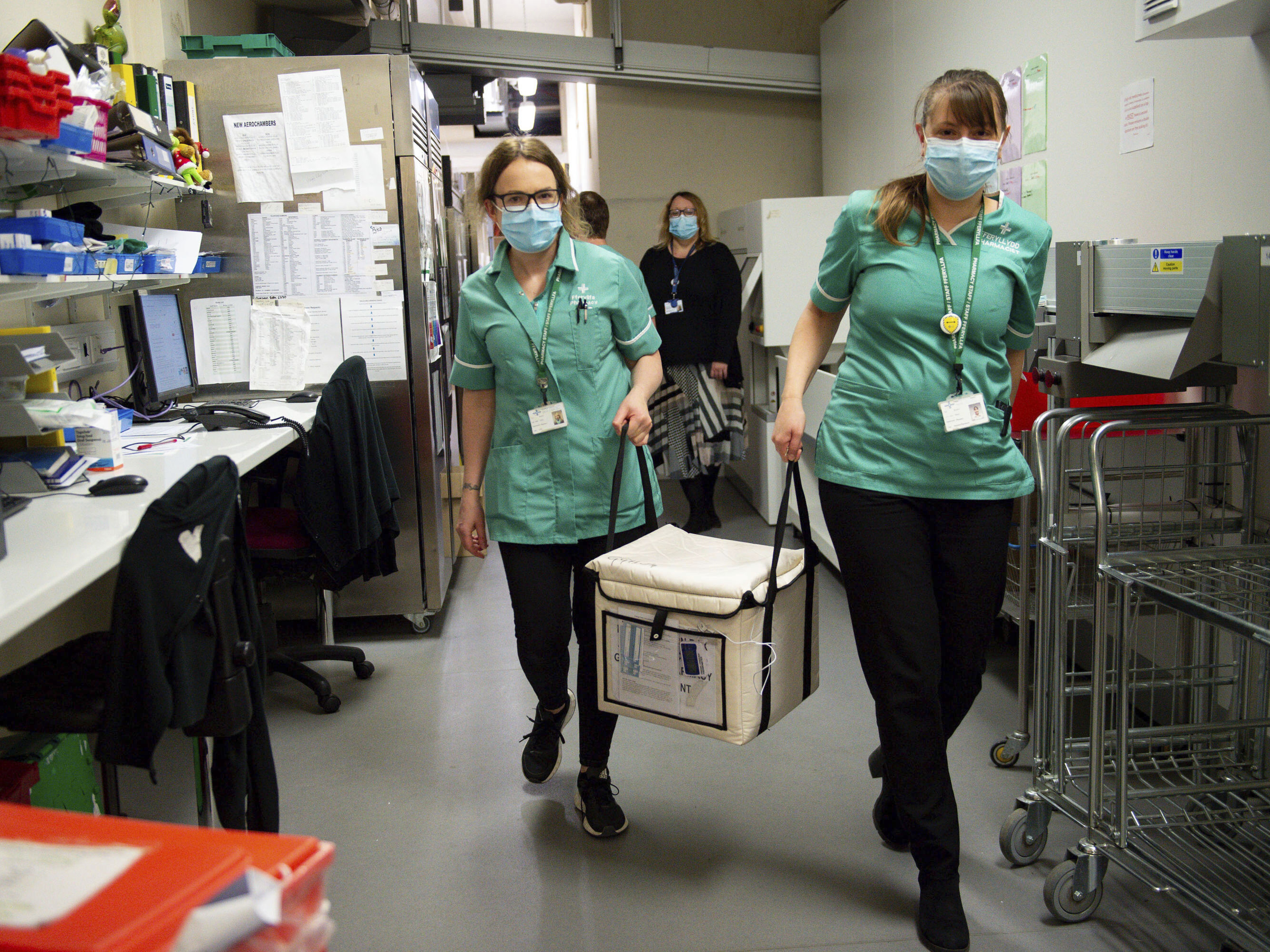 caption: On Wednesday, pharmacists at the West Wales General Hospital in Carmarthen, Wales, transport a cool box containing the first batch of Moderna vaccines being distributed in Britain.