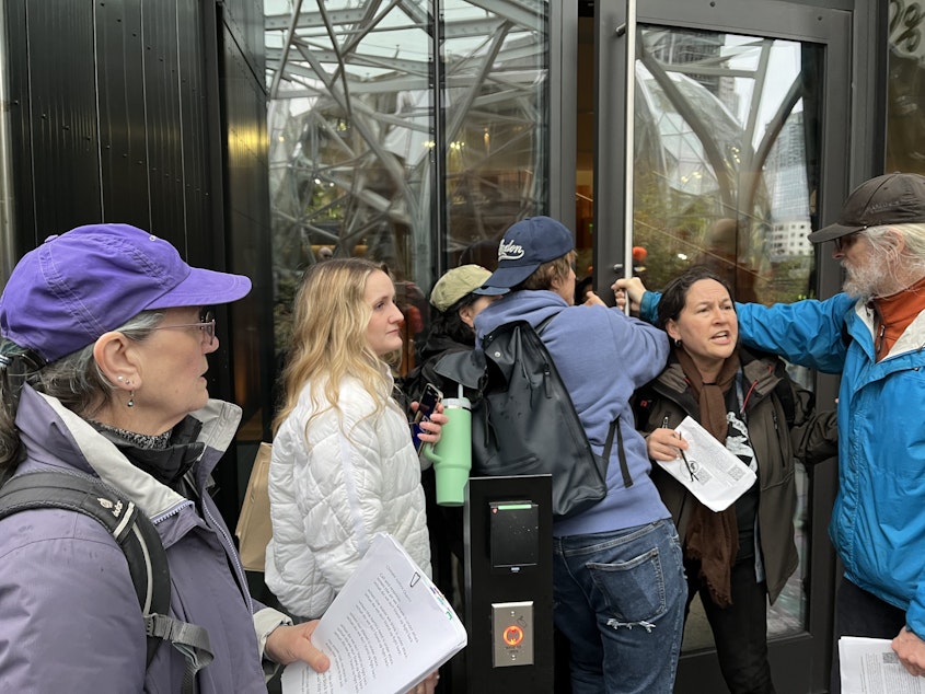 caption: Amazon employees try to make their way around climate protesters blocking the entrance to the company's Seattle headquarters March 27, 2024. 