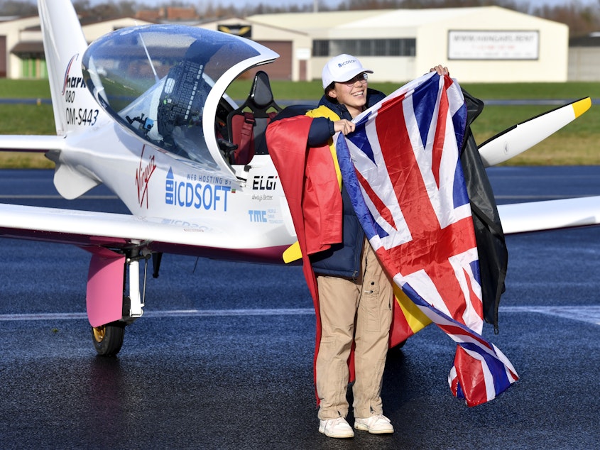 caption: Zara Rutherford, 19, carries the Belgian and British flags on the tarmac after landing her Shark ultralight plane at the Kortrijk airport in Belgium, on Thursday at the completion of a record-breaking solo circumnavigation.