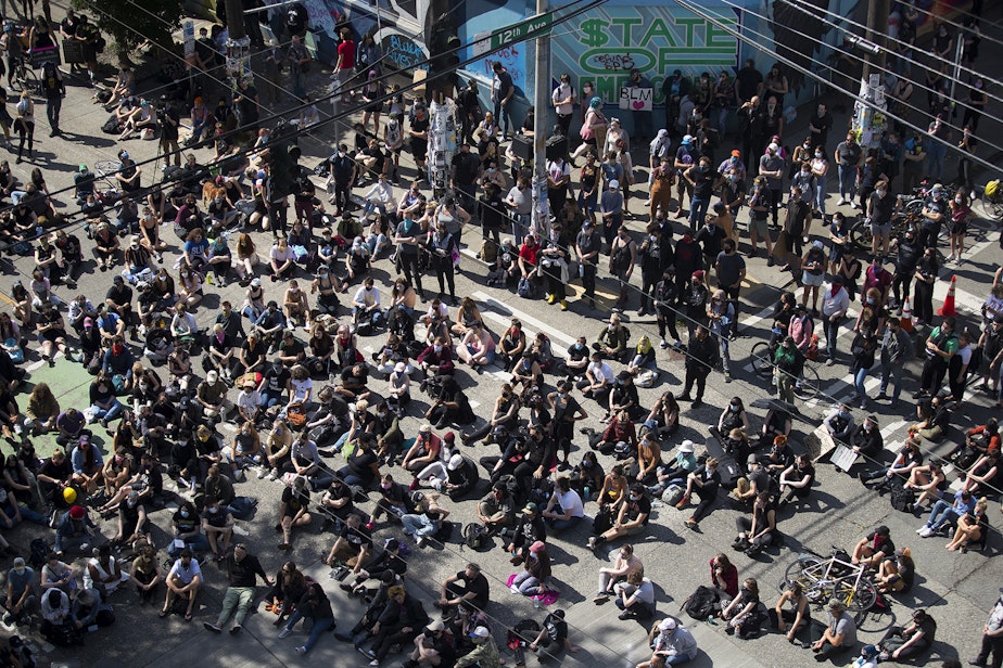 caption: A large crowd gathers at the intersection of East Pine Street and 12th Avenue, outside of the Seattle police department's East Precinct building, to listen to speakers on Wednesday, June 10, 2020, in Seattle.