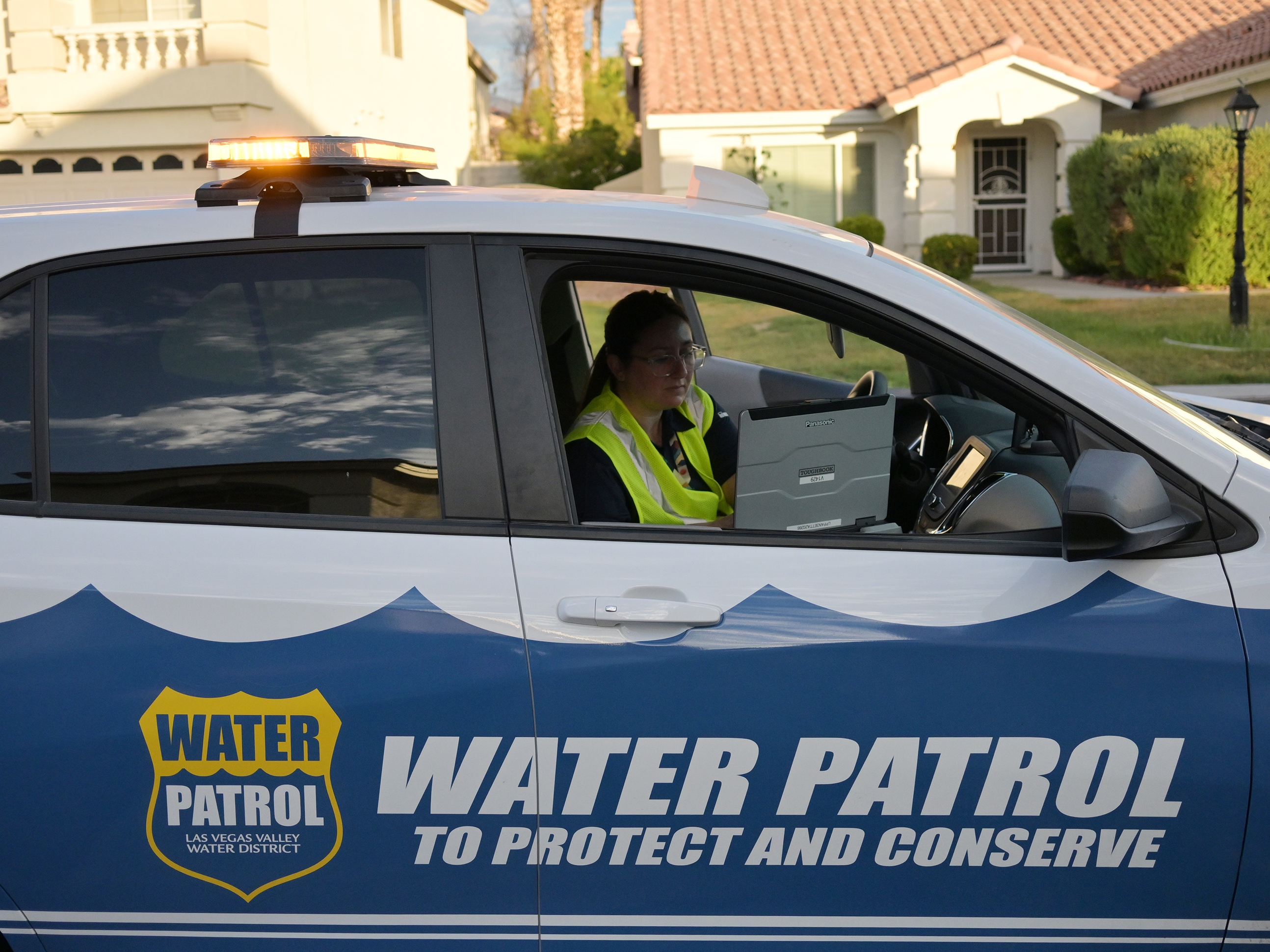caption: Las Vegas Valley Water District Water Waste Investigator Devyn Choltko puts a water waste violation into the computer system outside a home in north Las Vegas, Nevada, on June 25, 2024.  Choltko is one of more than a dozen investigators who patrol Las Vegas neighborhoods looking for water being wasted during irrigation times.