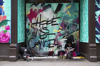caption: Marty Jackson, left, and Gracie Ann, right, sit in the doorway of a boarded up business in front of a mural that reads 'Hope is Not Cancelled,' on Tuesday, April 28, 2020, along First Avenue South in Seattle. 