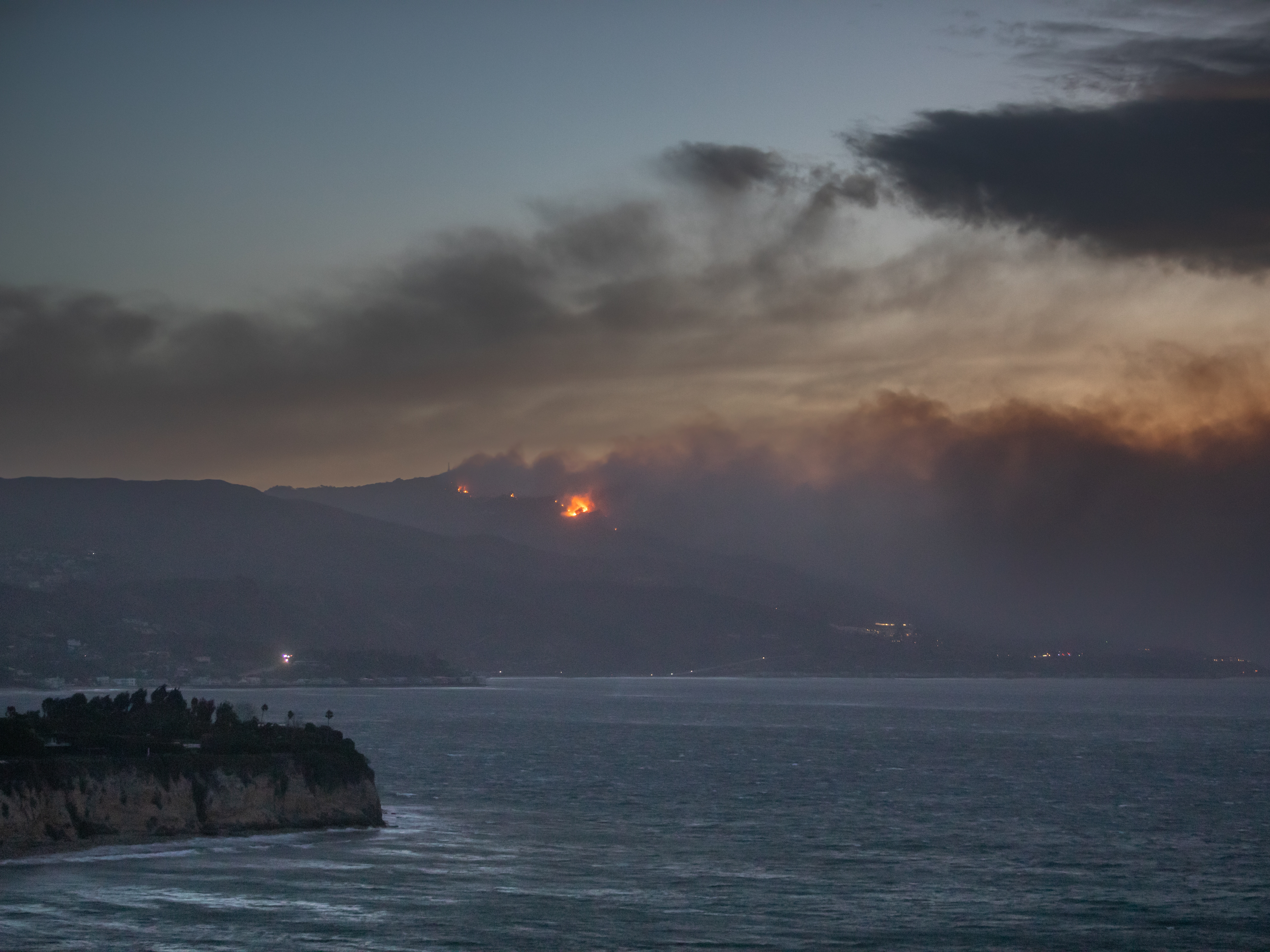 caption: Smoke from the Palisades Fire is seen from Point Dume while it burns homes along the Pacific Coast Highway amid a powerful windstorm on Wednesday in Malibu, California. Fueled by intense Santa Ana winds, the Palisades Fire has burned through thousands of acres while a second major fire continues to burn near Eaton Canyon in Altadena.