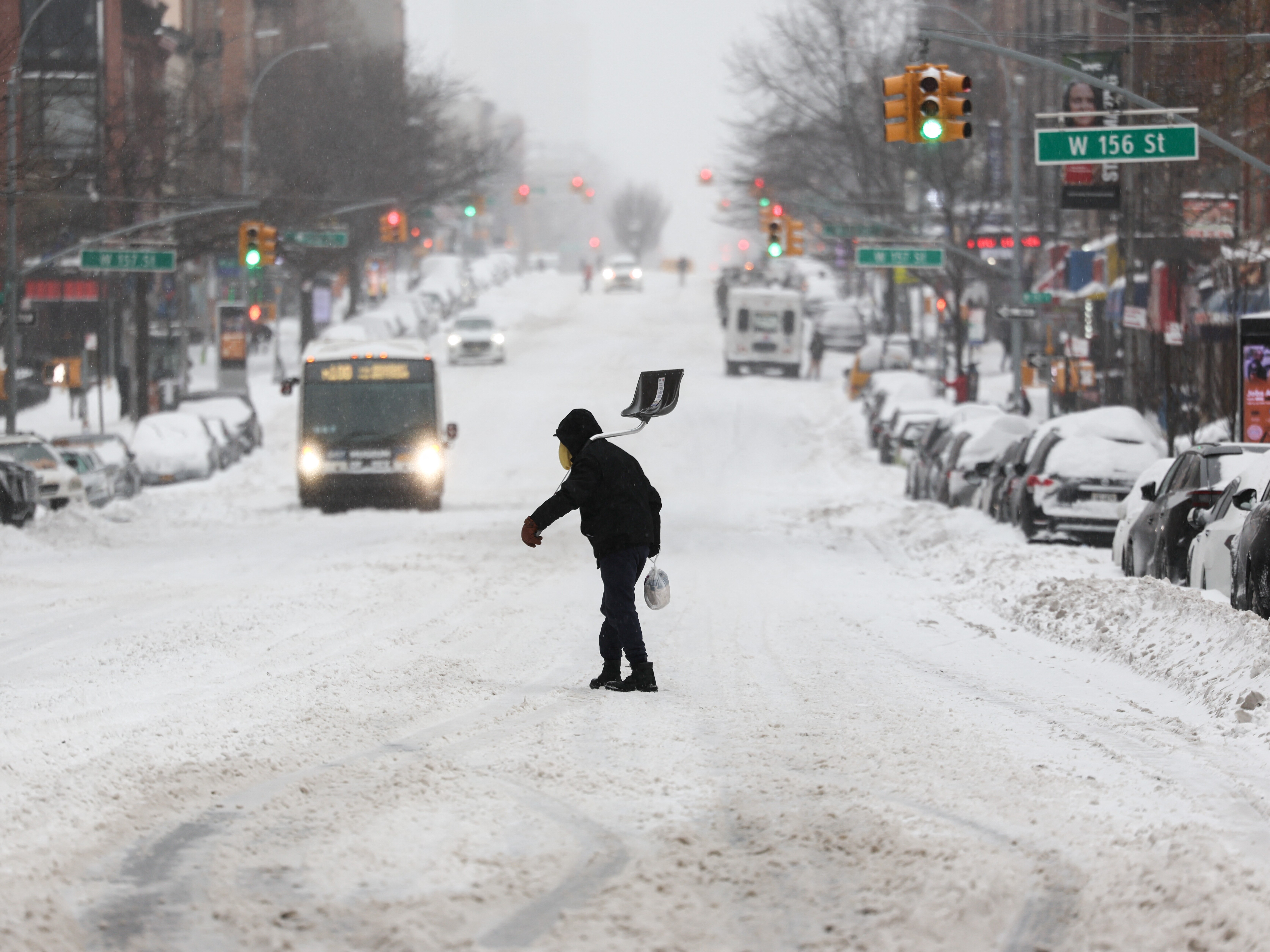 caption: A man carries a shovel as he crosses a street in the Hamilton Heights neighborhood in New York on Sunday.