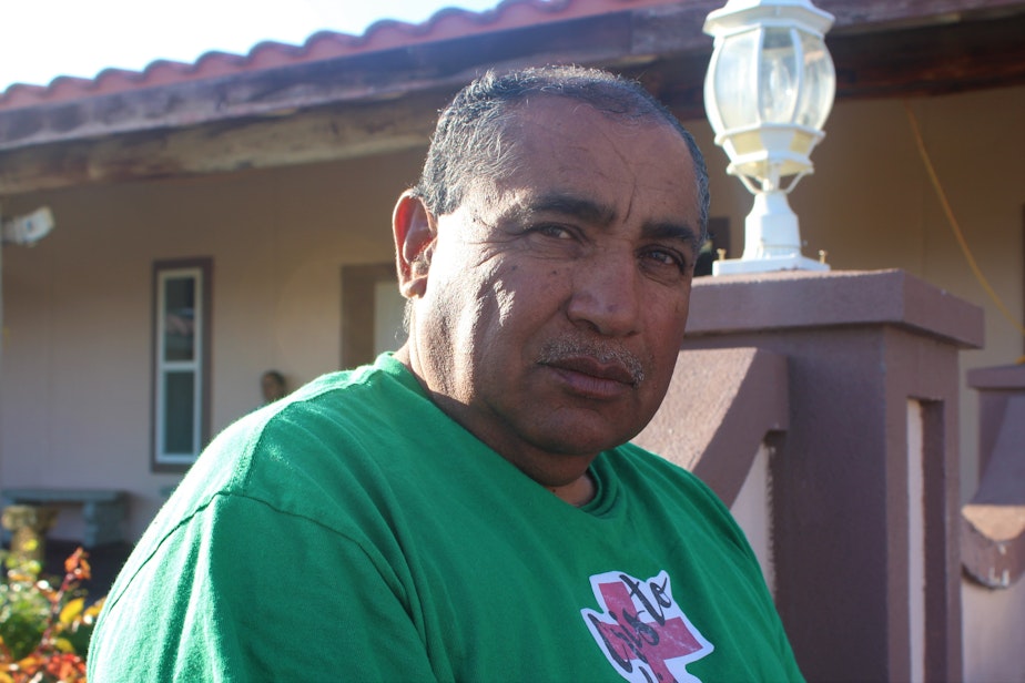caption: Sergio Rodriguez sits in the warm spring sunlight outside of the Our Lady of the Desert Parish catholic church in Mattawa, in central Washington. He says the workers help raise local wages about a dollar when they come to town, but they also get to take more of their paycheck home.