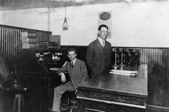 caption: UPS founders Jim Casey and Claude Ryan in their office at 123 Marion Street, Seattle, in 1910.  The company, then American Messenger Company, delivered phone messages, beer, medicine, and food by foot and bicycle.