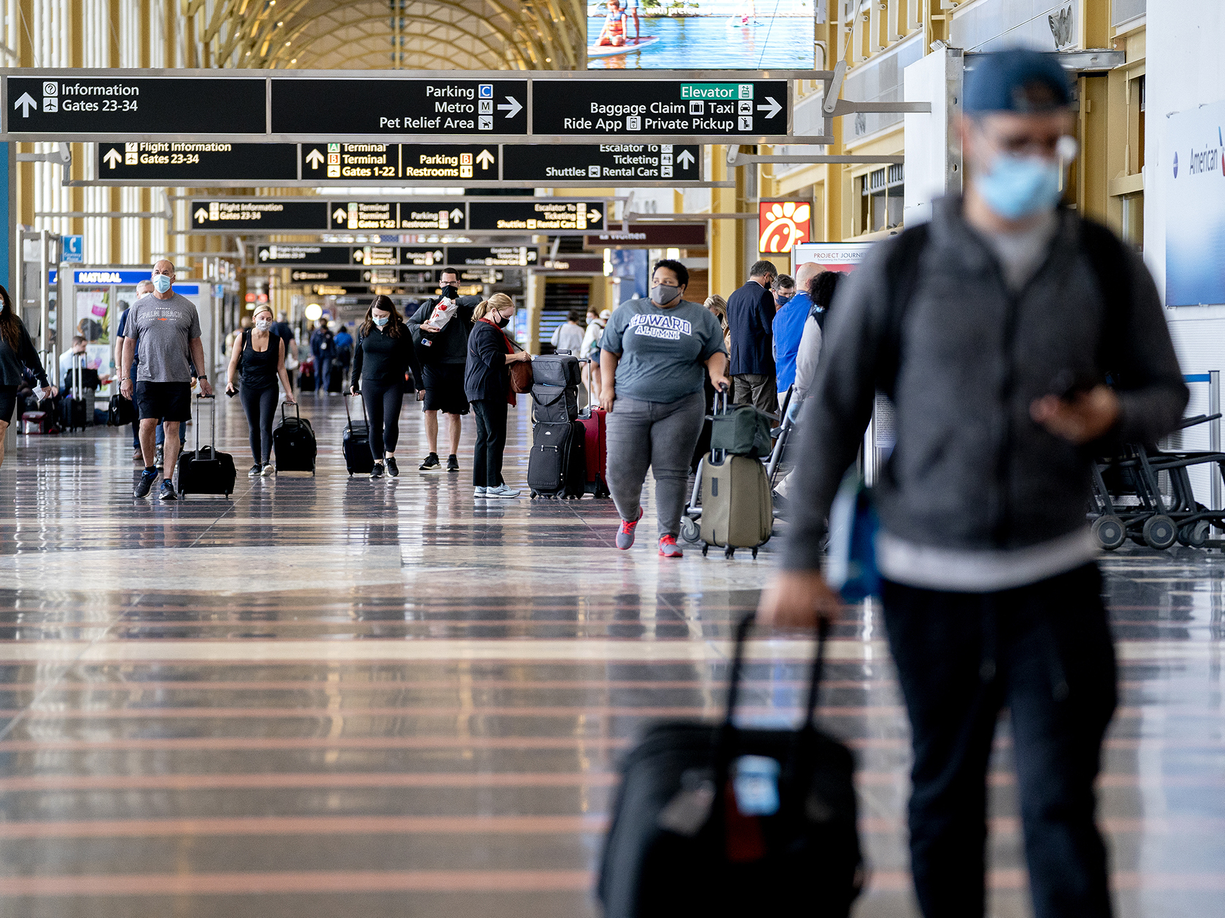 caption: Travelers wearing protective masks walk through Ronald Reagan National Airport in Arlington, Va., in May.
