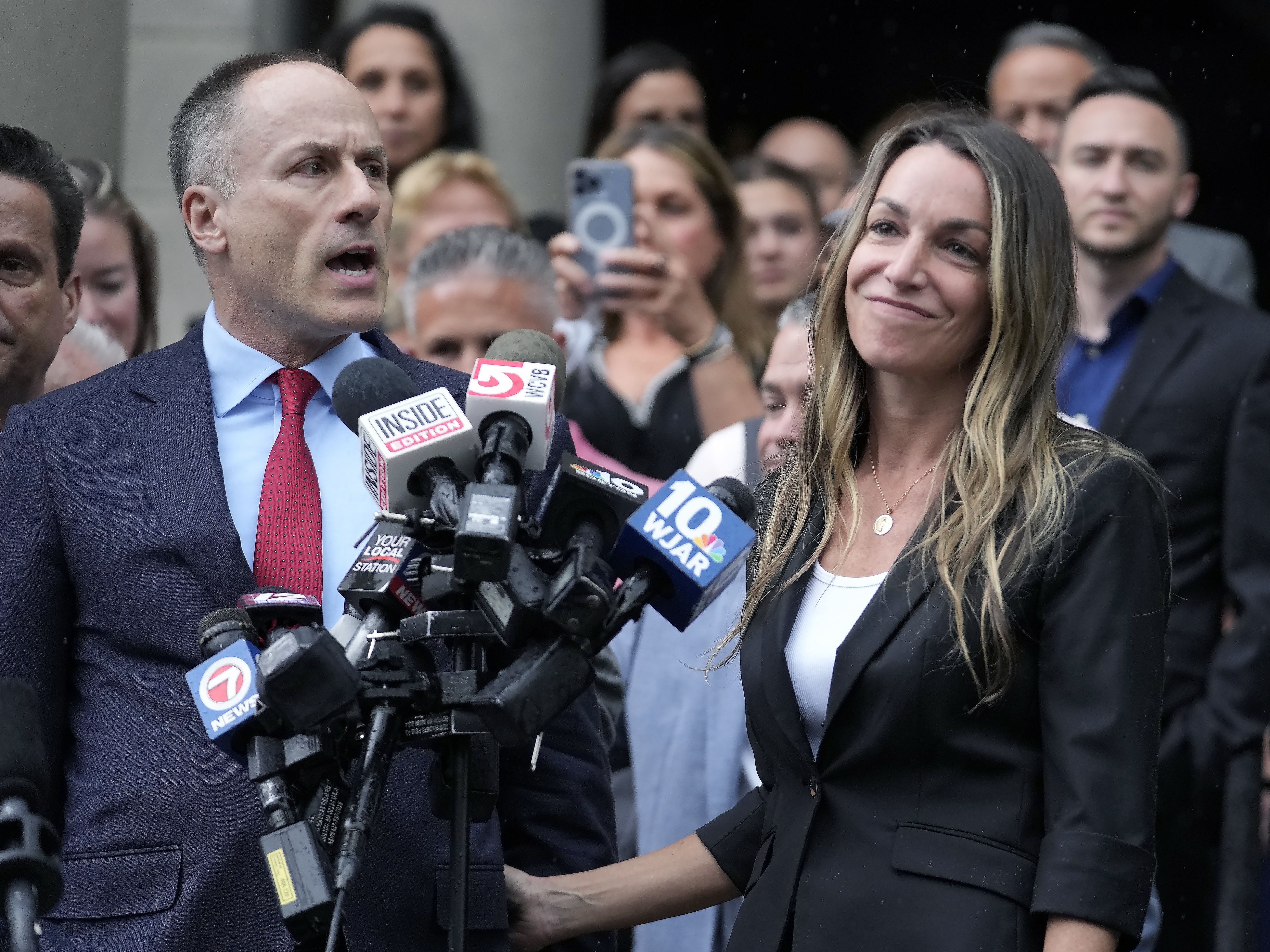 caption: Karen Read, right, smiles as defense attorney David Yannetti, front left, speaks to reporters in front of Norfolk Superior Court in Dedham, Mass., after the judge declared a mistrial on Monday.